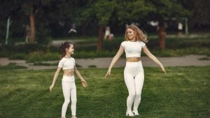 Mother and daughter bonding through outdoor exercise in activewear, featuring a joyful moment in a green park.